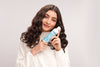 Model with loose brown curls holding a bottle of Moisture Lock® Leave-In Conditioner near their face