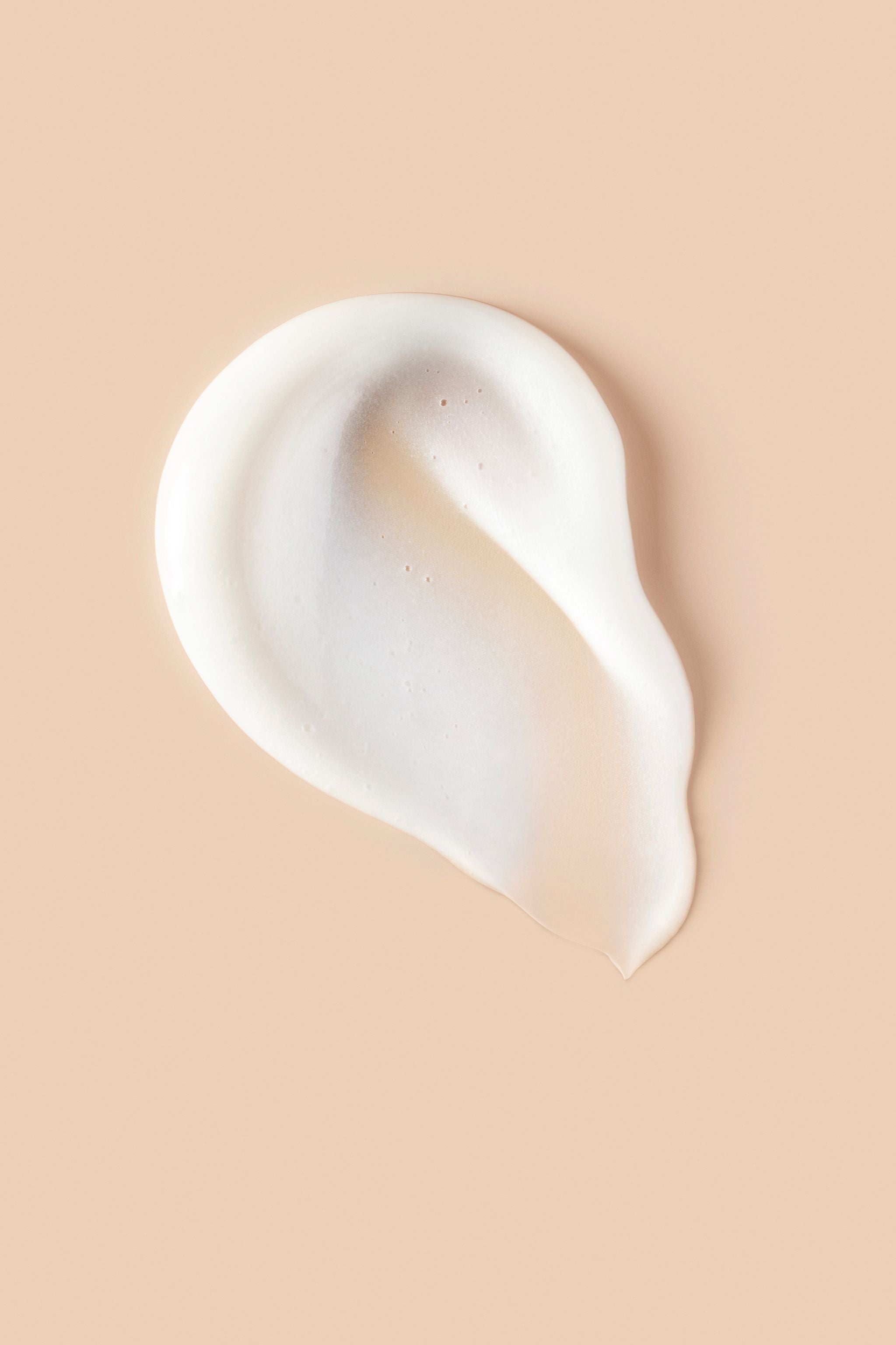 Portion of white Curl Shaper Double Duty Weightless Cleansing Conditioner on beige background